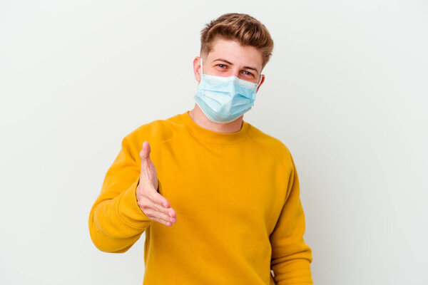 Young man wearing a mask for coronavirus isolated on white background stretching hand at camera in greeting gesture.
