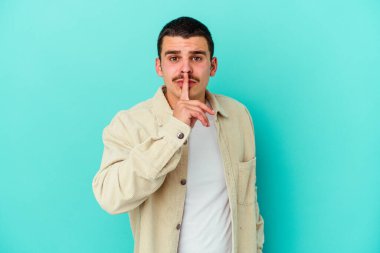 Mavi arka planda izole edilmiş genç beyaz bir adam ya sır saklıyor ya da sessizlik istiyor..