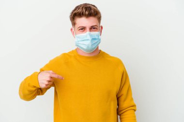 Coronavirus maskesi takan genç bir adam beyaz arka planda izole edilmiş, gömlek fotokopi alanını işaret eden, gururlu ve kendinden emin.