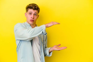 Sarı arka planda izole edilmiş genç beyaz adam elleri arasında bir kopya alanı tutarken şok ve hayrete düştü..