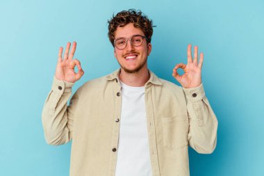 Gözlüklü genç beyaz adam mavi arka planda izole edilmiş neşeli ve kendinden emin..