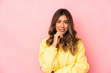 Kafkasyalı genç bir kadın yalnız, mutlu ve kendinden emin gülümsüyor, elleriyle çenesine dokunuyor..