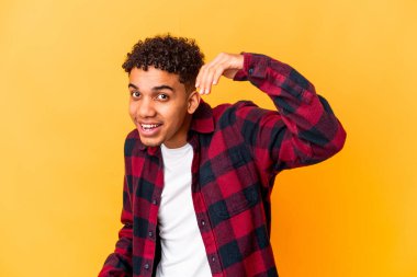 Genç Afro-Amerikalı kıvırcık adam, mor üzerine izole edilmiş, bir şeye gülüyor, elleriyle ağzını kapatıyor..