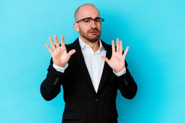 Genç, beyaz, kel bir adam mavi arka planda izole edildi. Tehlike nedeniyle şok oldu.