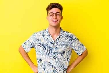 Sarı arka planda izole edilmiş genç beyaz adam ellerini kalçalarına koyuyor..