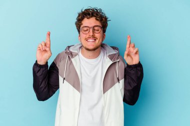 Gözlüklü genç beyaz adam mavi arka planda izole edilmiş şans dilemek için şans diliyor.