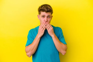 Sarı arka planda izole edilmiş genç beyaz adam elleriyle ağzını kapatırken şok oldu..