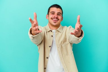 Mavi arka planda izole edilmiş genç beyaz adam kameraya sarıldığı için kendinden emin hissediyor..