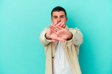 Kafkasyalı genç adam mavi arka planda izole edilmiş bir şekilde inkar hareketi yapıyor.