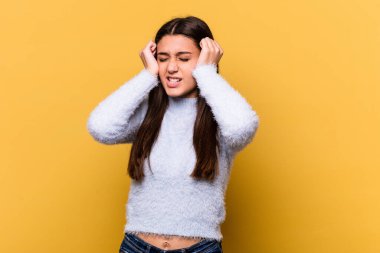 Sarı arka planda izole edilmiş genç Hintli kadın elleriyle kulakları örtüyor..