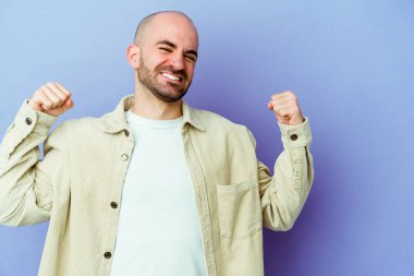 Mor arka planda izole genç, beyaz kel bir adam zaferden sonra yumruğunu kaldırıyor, kazanan konsept..