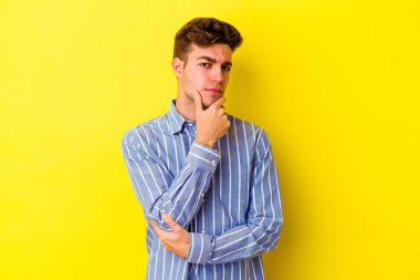 Genç beyaz adam sarı arka planda izole edilmiş şüpheli, belirsiz, seni muayene ediyor..