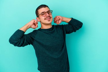 Mavi arka planda izole edilmiş genç beyaz adam kollarını uzatıyor, rahat bir konumda..