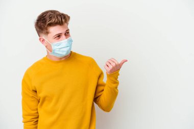 Koronavirüs için maske takan genç adam beyaz arka planda izole edilmiş, baş parmak uzakta, gülen ve kaygısız..