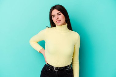 Mavi arka planda izole edilmiş beyaz bir kadın sırt ağrısı çekiyor..