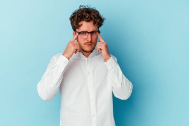 Kafkasyalı genç iş adamı mavi arka planda izole edilmiş bir göreve odaklanmış, işaret parmaklarını işaret ediyor..