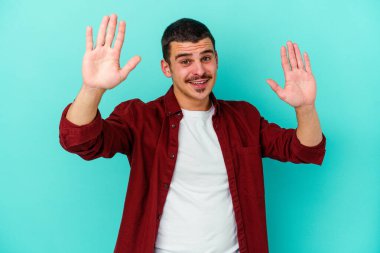 Mavi arka planda izole edilmiş genç beyaz adam hoş bir sürpriz alıyor, heyecanlı ve el kaldırıyor..