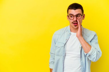 Sarı arka planda izole edilmiş genç beyaz adam gizli bir sıcak fren haberi veriyor ve yana bakıyor.