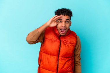 Genç Afro-Amerikalı kıvırcık adam mavi üzerine izole edilmiş yüksek sesle bağırıyor, gözlerini açık ve ellerini gergin tutuyor..