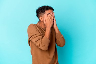 Genç Afro-Amerikan kıvırcık adamı mavi üzerine izole edilmiş, gözleri korkuyla kaplı, elleriyle..