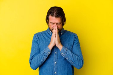 Sarı arka planda izole edilmiş orta yaşlı beyaz bir adam el ele tutuşup dua ederken kendine güveniyor..