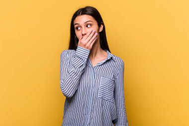 Genç Hintli bir kadın sarı arka planda izole edilmiş. Düşünceli bir şekilde bir fotokopi odasına bakıyor. Ağzını eliyle kapatıyor..