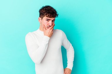 Kafkasyalı genç adam mavi arka planda izole edilmiş ağzı kapalı ve elleri endişeli görünüyor..