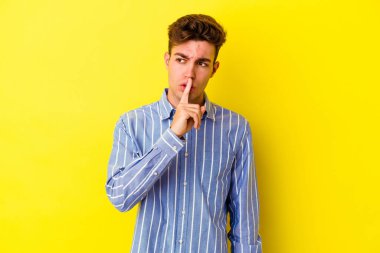 Sarı arka planda izole edilmiş genç beyaz bir adam ya sır saklıyor ya da sessizlik istiyor..