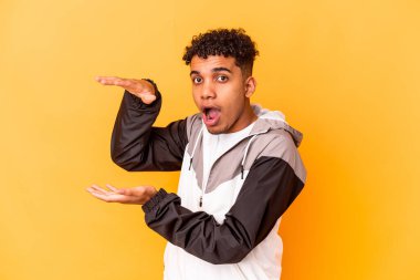 Genç Afro-Amerikan kıvırcık adamı, mor renkte izole edilmiş, şok olmuş ve hayret içinde, elleri arasında bir kopya alanı tutuyor..