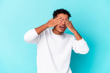 Genç Afro-Amerikan kıvırcık adamı mavi üzerine izole edilmiş, gözleri korkuyla kaplı, elleriyle..