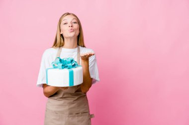 Genç Rus fırıncı kadın nefis bir pasta tutuyor dudaklarını katlıyor ve hava öpücüğü vermek için avuç içleri tutuyor..