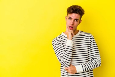 Sarı arka planda izole edilmiş genç beyaz adam şüpheli ve şüpheci bir ifadeyle yana bakıyor..