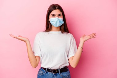 Pembe arka planda izole edilmiş virüs maskesi takan beyaz bir kadın kollarıyla ölçek oluşturuyor, mutlu ve kendinden emin hissediyor..