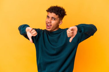 Genç Afro-Amerikalı kıvırcık adam, mor üzerine izole edilmiş, baş parmağını aşağı gösteren ve hoşlanmadığını ifade eden..