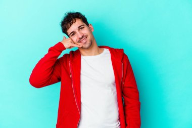 Mavi arka planda izole edilmiş genç beyaz adam parmaklarıyla bir cep telefonu hareketi gösteriyor..