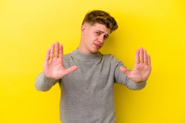 Sarı arka planda izole edilmiş genç beyaz adam elini uzatmış, dur işareti göstererek seni engelliyor..