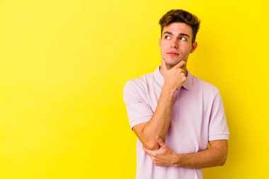 Sarı arka planda izole edilmiş genç beyaz adam şüpheli ve şüpheci bir ifadeyle yana bakıyor..