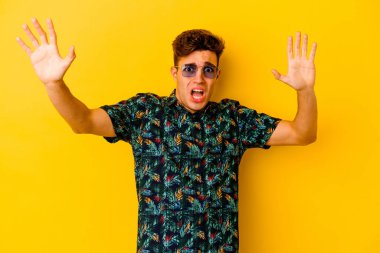 Hawaii tişörtü giyen genç beyaz adam sarı arka planda izole edilmiş. Yakın bir tehlike nedeniyle şok oluyor.