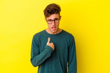 Sarı arka planda izole edilmiş genç beyaz adam parmağını göstererek şaşırdı ve gülümsedi..