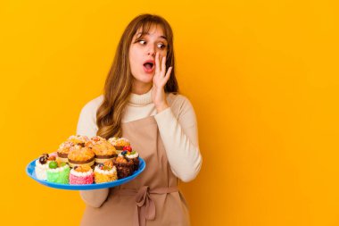 Sarı arka planda izole edilmiş genç pasta şefi kadın gizli bir sıcak fren haberi veriyor ve yana bakıyor.