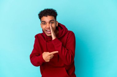 Genç Afro-Amerikan Kıvırcık Adam mavi üzerine izole edilmiş bir şekilde dedikodu yapıyor, bir şeyleri bildiriyor..