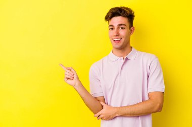 Sarı arka planda izole edilmiş genç beyaz adam işaret parmağıyla işaret ederek gülümsüyor..