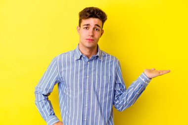 Sarı arka planda izole edilmiş genç beyaz adam sorgulama sırasında omuz silkiyor ve kuşkulanıyor..