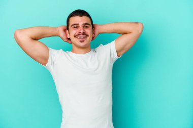 Mavi arka planda izole edilmiş genç beyaz adam kollarını uzatıyor, rahat bir konumda..