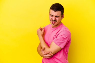 Kafkas asıllı genç adam sarı arka planda izole edilmiş dirsek masajı yapıyor, kötü bir hareketin ardından acı çekiyor..