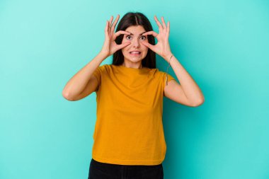 Mavi arka planda izole edilmiş genç beyaz kadın bir başarı fırsatı bulmak için gözlerini açık tutuyor..