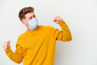 Coronavirus maskesi takan genç adam beyaz arka planda izole edilmiş zafer kazandıktan sonra yumruk kaldırıyor, kazanan konsept..