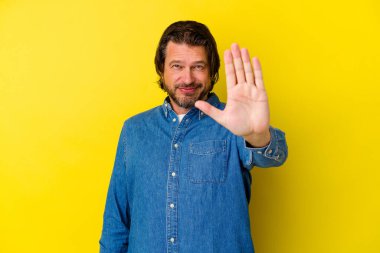 Orta yaşlı beyaz bir adam, sarı arka planda izole edilmiş, elini uzatmış, dur işareti göstererek, seni engelliyor..