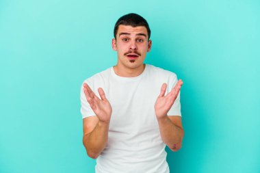 Kafkasyalı genç adam mavi arka planda izole edildi. Şaşırdı ve şok oldu..