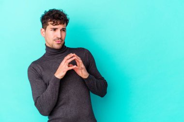 Kafkasyalı genç bir adam mavi arka planda izole edildi. Aklında bir plan kuruyor, bir fikir kuruyor..